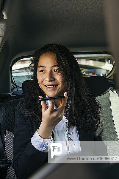 Porträt einer glücklichen Geschäftsfrau  die in einem Auto sitzt und ein Mobiltelefon benutzt