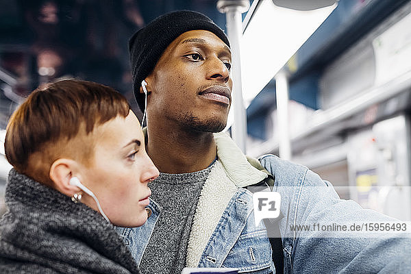 Porträt eines jungen Paares  das sich in einer U-Bahn Ohrstöpsel teilt
