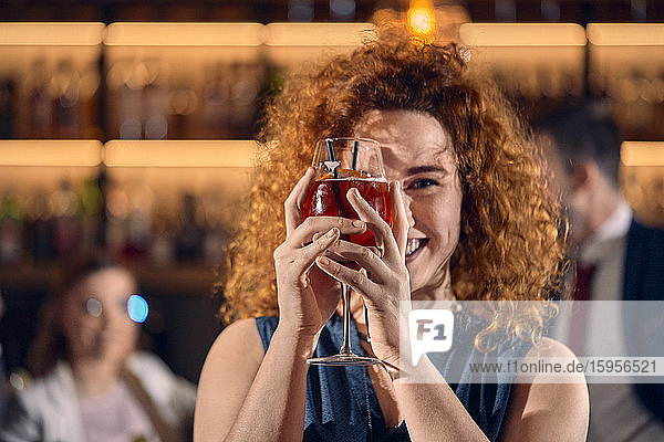 Porträt einer glücklichen jungen Frau  die in einer Bar ein Cocktailglas hält