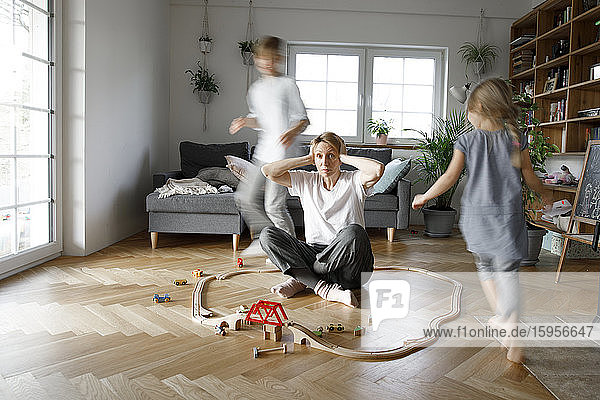 Stressed out mother sitting in the middle of toys  while children are running around her