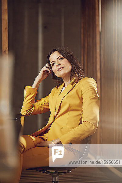 Porträt einer selbstbewussten Geschäftsfrau im gelben Anzug am Schreibtisch im Büro sitzend