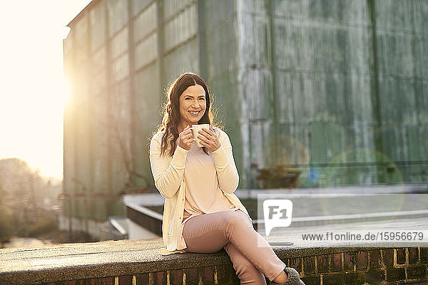 Zuversichtlich lächelnde  reife Geschäftsfrau beim Kaffeetrinken auf einer Terrasse in der Stadt