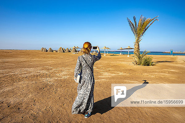 Ägypten  Hurghada  Touristin beim Fotografieren von Sonnenschirmen und Strohhütten an der Küste der Sahl-Haschisch-Bucht