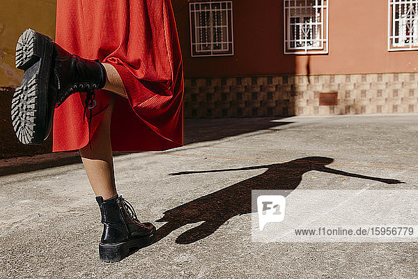 Junge Frau in rotem Kleid und schwarzen Stiefeln,  die mit ihrem Schatten auf dem Boden spielt