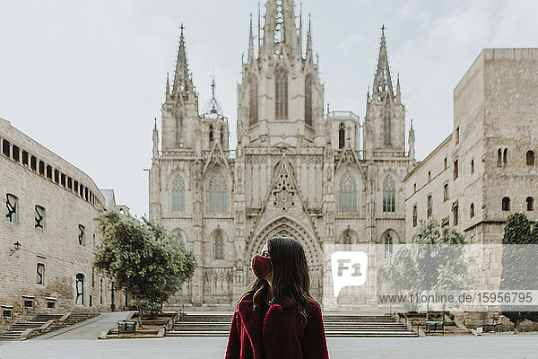 Frau mit Gesichtsmaske schaut weg  während sie während der Quarantäne gegen die Kathedrale von Barcelona steht  Barcelona  Spanien