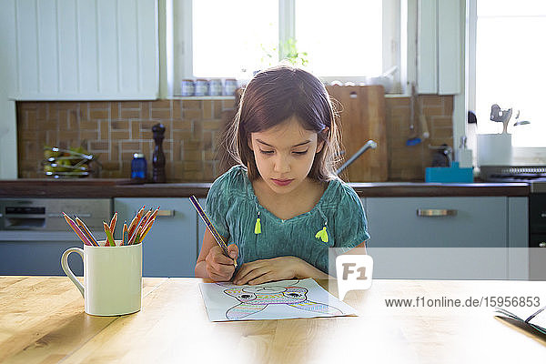 Kleines Mädchen sitzt am Küchentisch und zeichnet einen Osterhasen