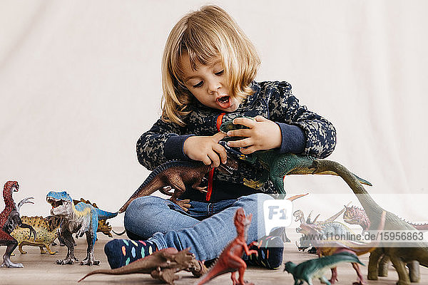 Porträt eines kleinen Mädchens  das auf dem Boden sitzt und mit Spielzeug-Dinosauriern spielt