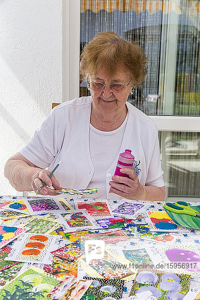 Porträt einer glücklichen älteren Frau  die auf einer Terrasse malt