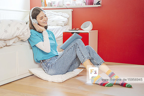 Porträt eines lächelnden Teenager-Mädchens mit geschlossenen Augen  das mit Kopfhörer und digitalem Tablett Musik hört
