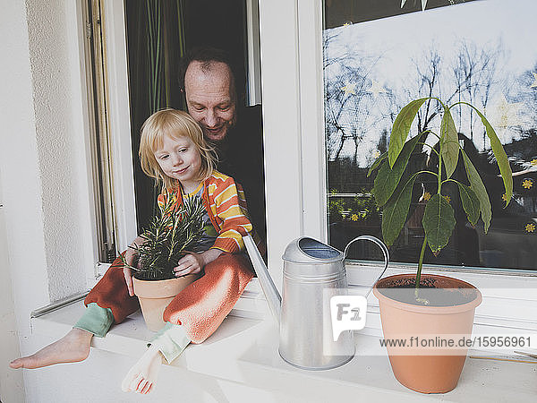 Father with daughter sitting on windowsill by potted plant