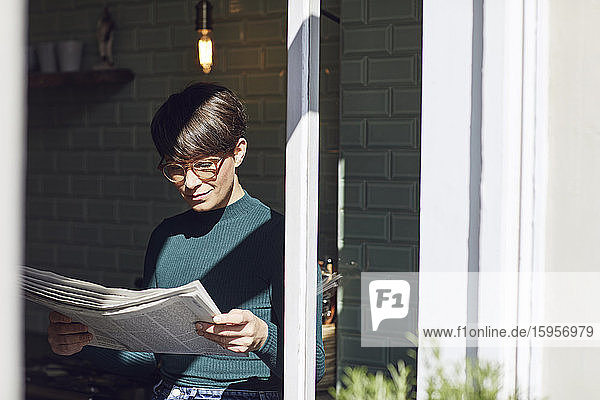 Frau steht zu Hause am Fenster und liest Zeitung
