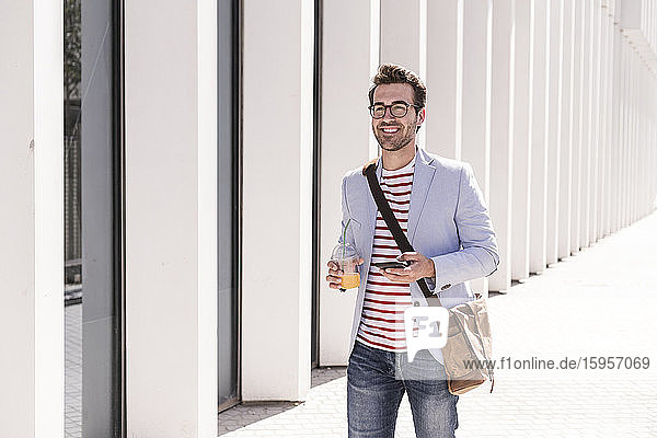 Smiling young man in the city with cell phone and takeaway drink  Lisbon  Portugal