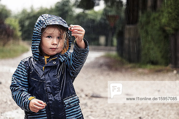 Bildnis eines kleinen Mädchens mit Schnecken in den Händen im Regen stehend