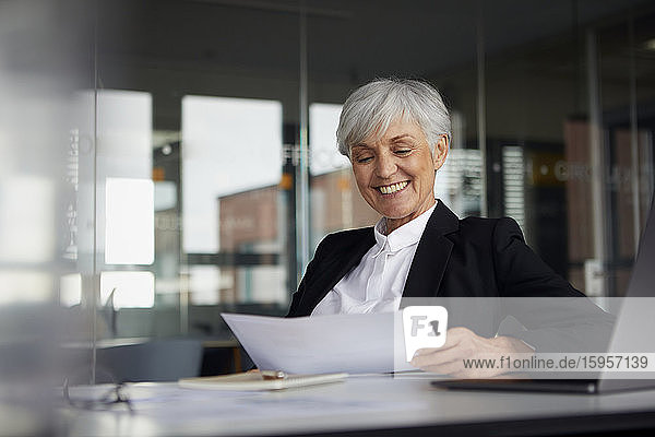 Porträt einer lächelnden älteren Geschäftsfrau  die am Schreibtisch sitzt und sich Dokumente ansieht