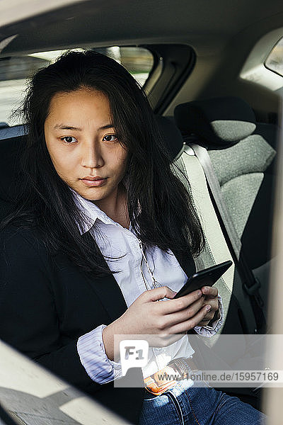 Porträt einer nachdenklichen Geschäftsfrau mit Mobiltelefon  die in einem Auto sitzt und in die Ferne schaut