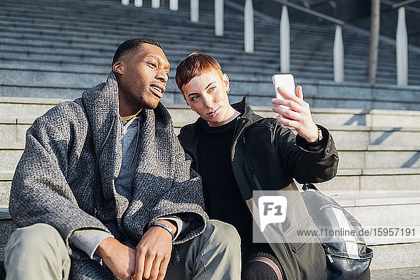 Young couple sitting on stairs in the city taking a selfie