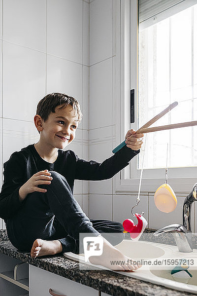 Porträt eines glücklichen Jungen beim Angeln von Gummienten in der Küchenspüle
