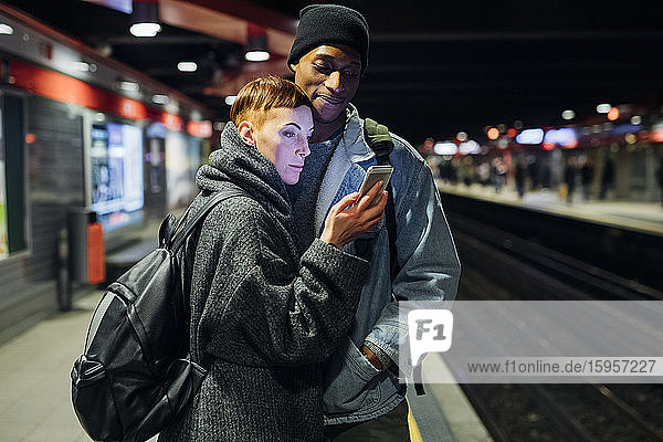 Junges Paar teilt sich ein Smartphone auf dem Bahnsteig