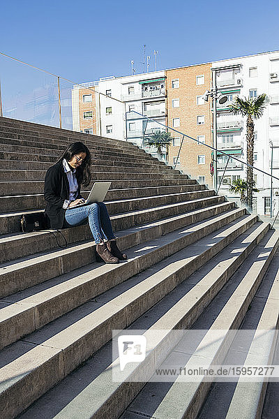 Junge Geschäftsfrau sitzt mit Laptop auf einer Treppe im Freien