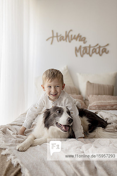 Porträt eines glücklichen kleinen Jungen im Bett mit seinem Hund