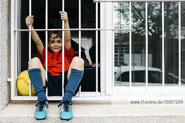 Junge mit Fussball am Fenster  ohne das Haus zum Spielen verlassen zu können
