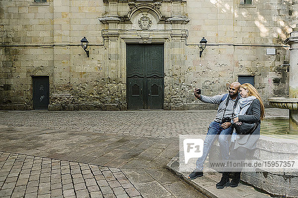 Ein Paar  das sich mit einem Smartphone selbstständig macht  auf dem Platz Sant Felip Neri  Barcelona  Spanien