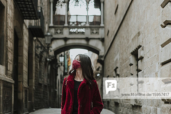 Frau mit Gesichtsmaske schaut weg  während sie während der Quarantäne in einer leeren Gasse des Gotischen Viertels steht  Barcelona  Spanien