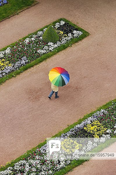 Person mit Regenschirm in Regenbogenfarben auf einem roten Kiesweg zwischen Blumenrabatten im Schlosspark Stadtschloss Fulda Hessen Deutschland Europa