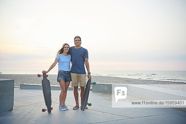 A young couple  man and woman skateboarding by the beach at sunset.