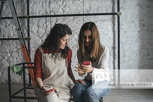 Zwei mittelgroße erwachsene Frauen schauen sich in ihrem neuen Geschäft ein Smartphone an