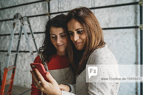 Zwei mittelgroße erwachsene Frauen  die in ihrem neuen Geschäft mit Smartphones Selbsthilfe betreiben