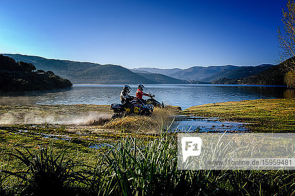 Two people riding motorcycles through shallows on Gusana lake  an artificial lake in the territory of Gavoi  Sardinia  Italy.