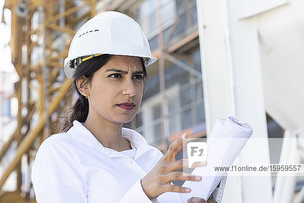 Architektin mit weißem Schutzhelm bei der Arbeit auf der Baustelle.