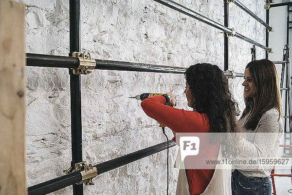 Zwei mittelgroße erwachsene Frauen bohren Wand in ihrem neuen Laden