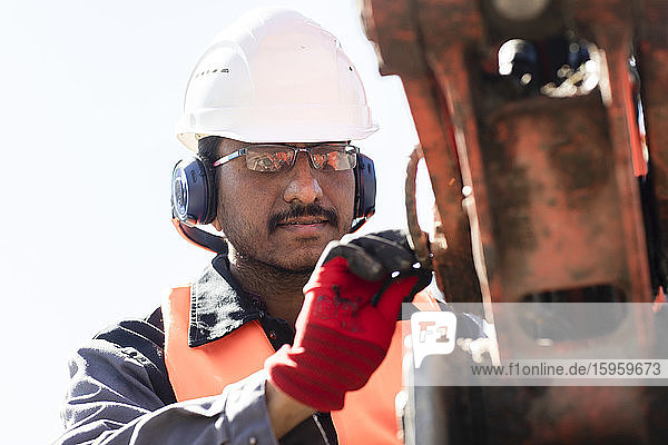 Männlicher Ingenieur mit Schutzhelm und Gehörschutz bei der Arbeit auf der Baustelle.