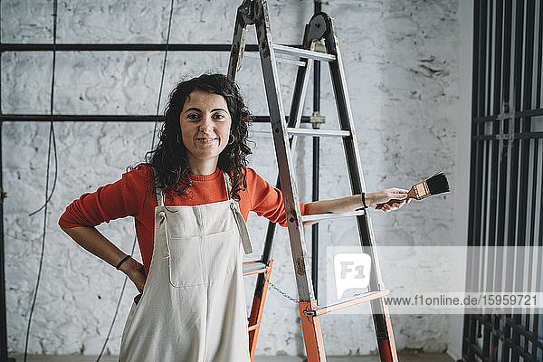 Mittelgroße erwachsene Frau  die in ihrem neuen Geschäft mit Pinsel auf einer Trittleiter lehnt  Porträt