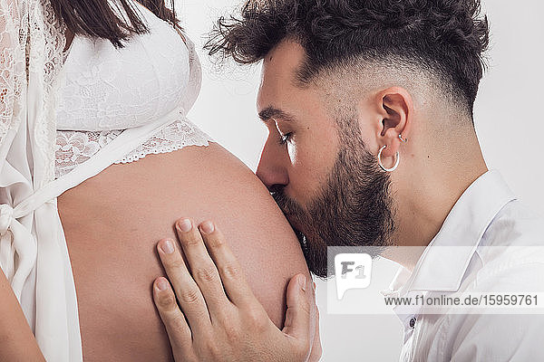 Bearded man kissing pregnant woman's bare stomach.