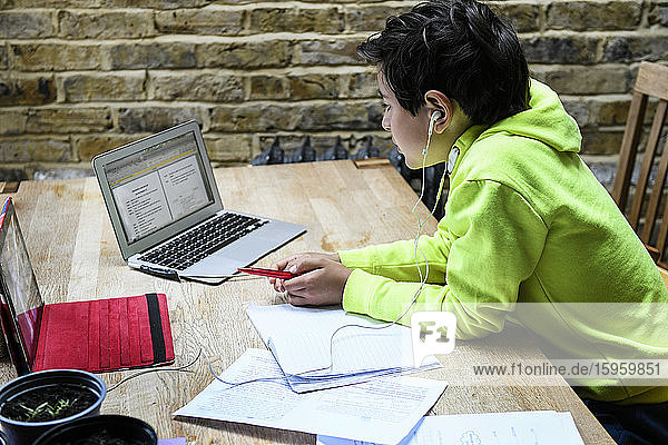 Ein Junge sitzt an einem Schreibtisch und benutzt einen Laptop für eine interaktive Lernsitzung Hausunterricht harte Arbeit.