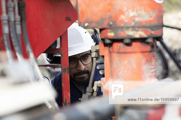Bärtiger Mann mit Brille und weißem Schutzhelm bei der Arbeit auf der Baustelle.