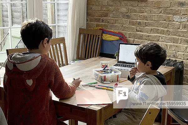 Two brothers seated at a table  drawing with felt pens  drawings to thank the NHS health service.