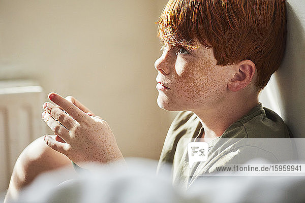 Boy with red hair sitting on floor in sunny room  holding game controller.