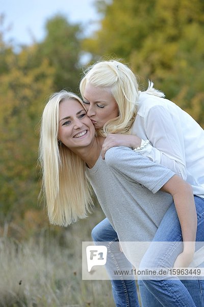 Fröhliche blonde junge Frau trägt ihre Freundin huckepack