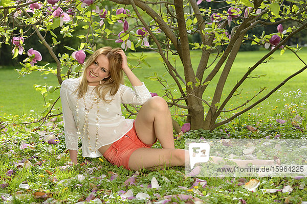 Junge Frau sitzt an einer blühenden Magnolie