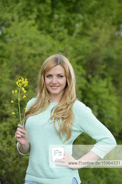 Blonde junge Frau hält eine Rapspflanze