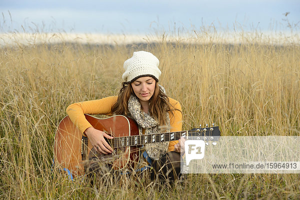 Young woman playing guitar in field