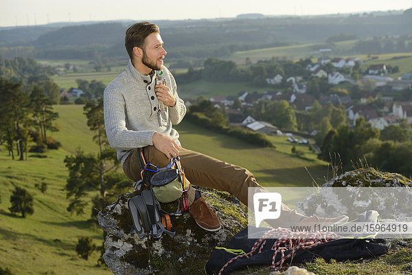 Mann sitzt auf einem Felsen mit Kletterausrüstung