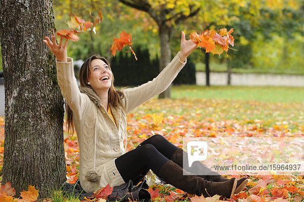 Glückliche junge Frau sitzt unter einem Baum im Herbst
