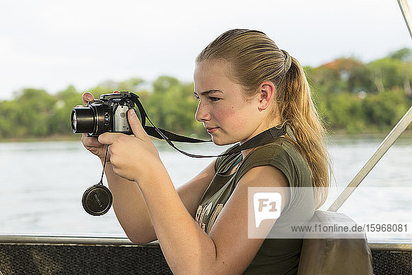 A twelve year old girl using a camera seated in a river boat.