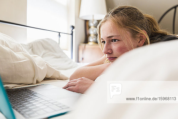 Teenagerin betrachtet Laptop im Bett