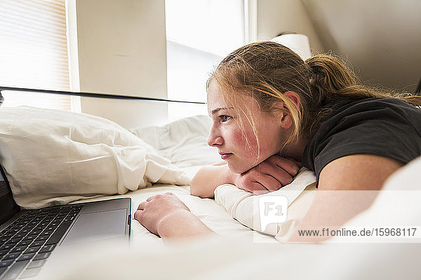 Teenagerin betrachtet Laptop im Bett